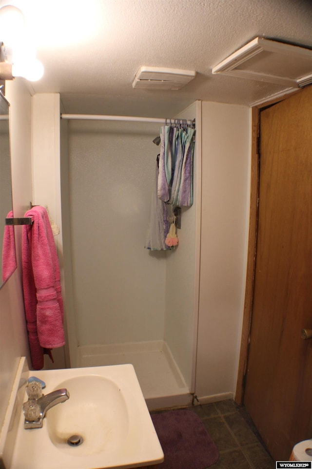 bathroom with a shower stall, a textured ceiling, a sink, and tile patterned floors