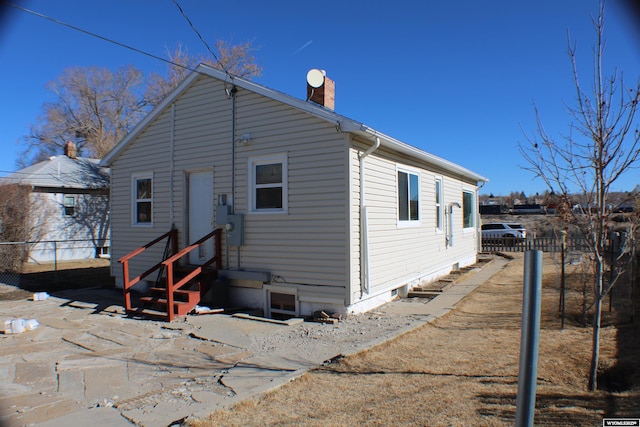 rear view of house featuring entry steps, a chimney, and fence