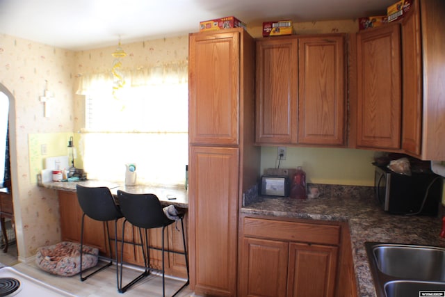 kitchen with arched walkways, brown cabinets, and wallpapered walls