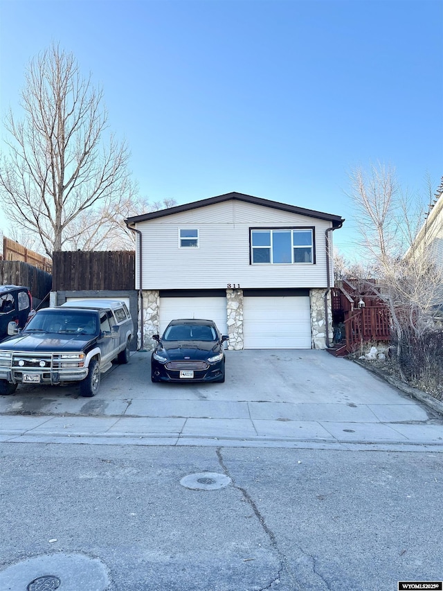 view of front of house with stone siding, an attached garage, fence, and driveway