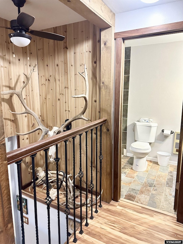 stairway with ceiling fan, wooden walls, and wood finished floors