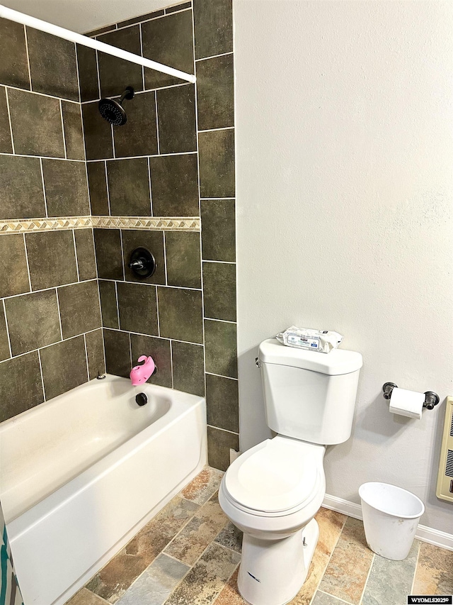 bathroom featuring toilet, stone tile floors, bathing tub / shower combination, baseboards, and heating unit