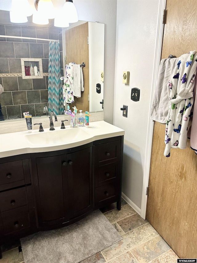 full bathroom featuring a shower with shower curtain, vanity, baseboards, tasteful backsplash, and stone tile flooring