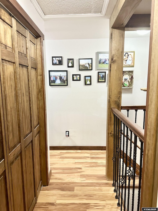 hallway with a textured ceiling, light wood-type flooring, an upstairs landing, and baseboards