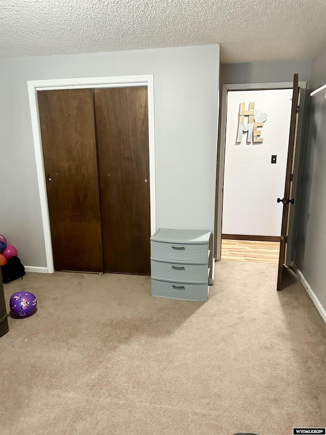 bedroom featuring a closet, light carpet, a textured ceiling, and baseboards