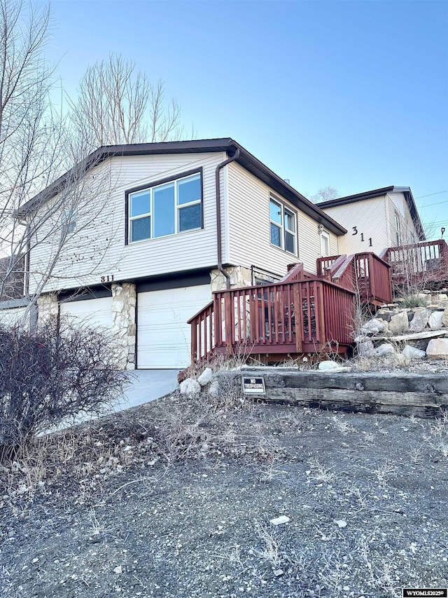 view of front of house with a garage, concrete driveway, a deck, and stone siding