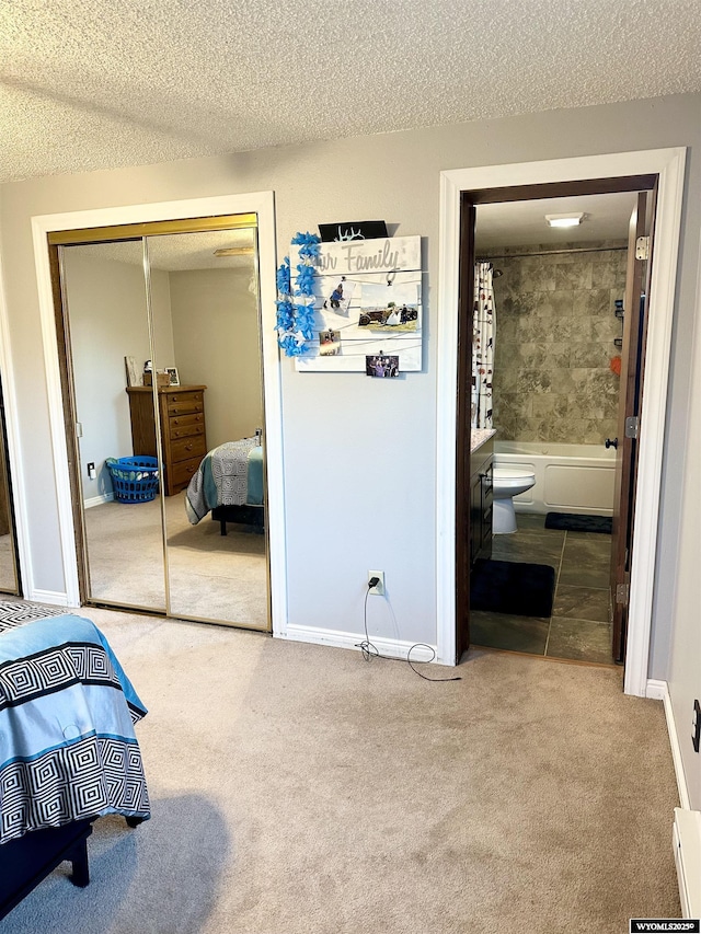 carpeted bedroom featuring a textured ceiling, baseboards, a closet, and ensuite bathroom