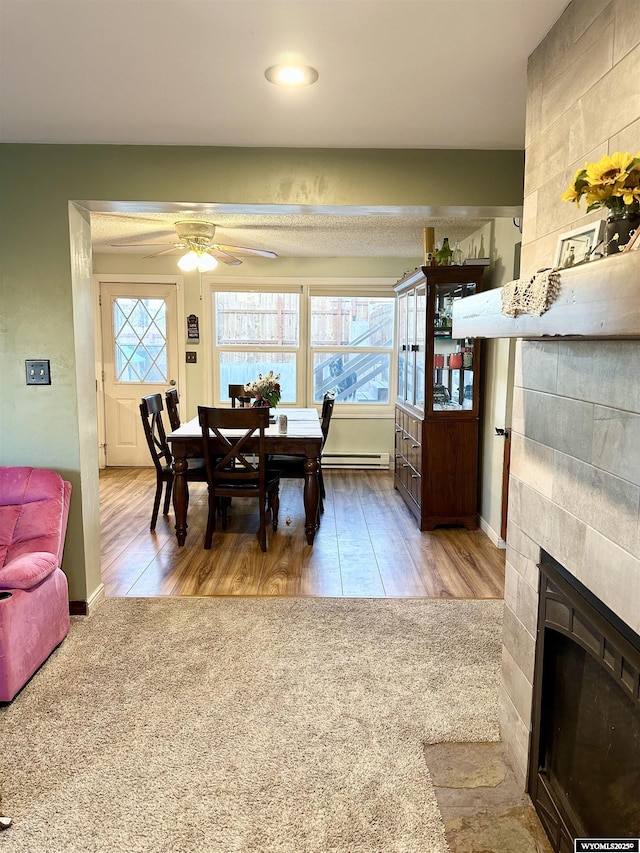 dining space with a baseboard radiator, wood finished floors, a ceiling fan, baseboards, and a tiled fireplace