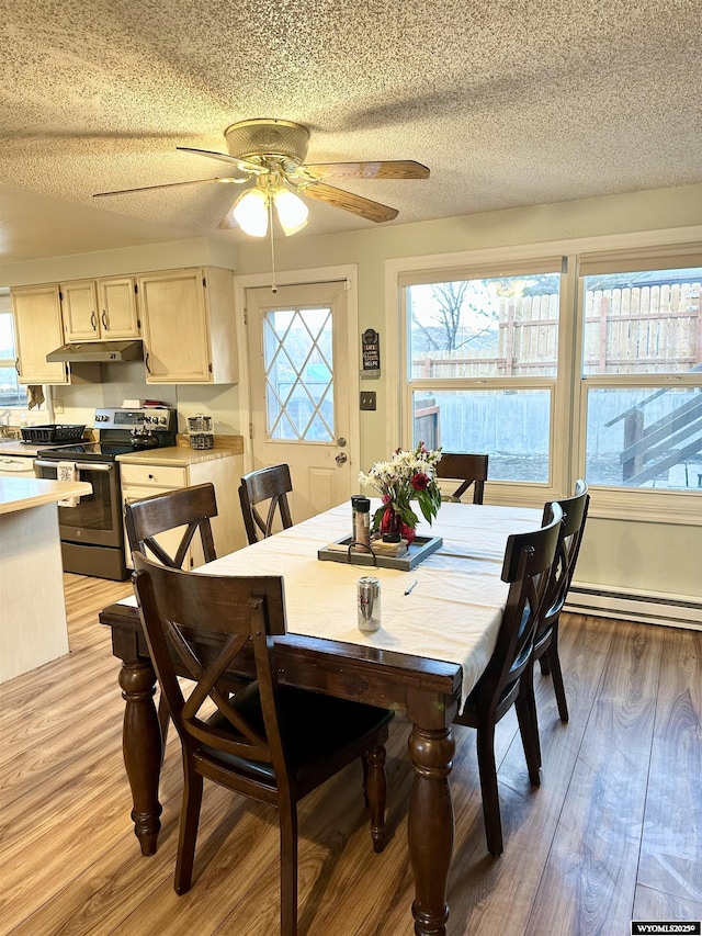 dining area with light wood finished floors, ceiling fan, a baseboard heating unit, and a textured ceiling