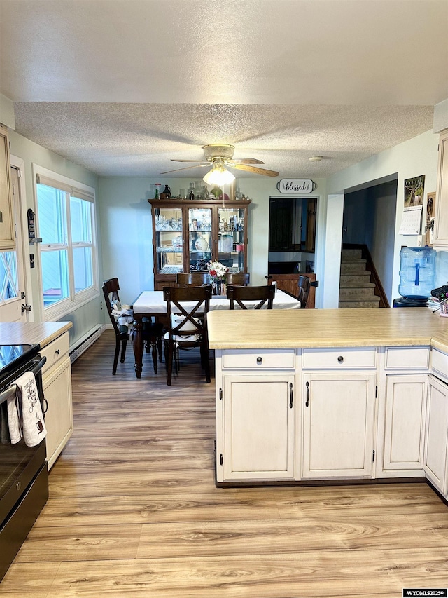 kitchen with a peninsula, light wood finished floors, baseboard heating, and black range with electric stovetop