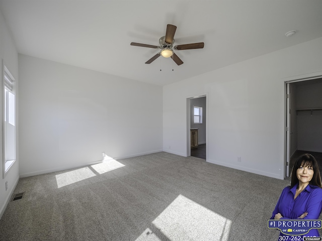 unfurnished bedroom featuring baseboards, multiple windows, a spacious closet, and carpet flooring