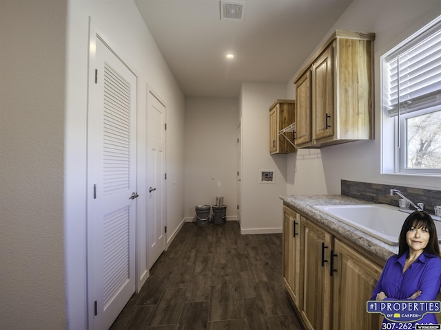 interior space with hookup for a washing machine, a sink, visible vents, baseboards, and dark wood-style floors