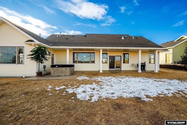 back of property with a shingled roof and a hot tub