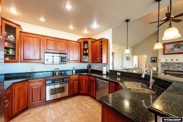 kitchen featuring lofted ceiling, appliances with stainless steel finishes, hanging light fixtures, a stone fireplace, and a sink