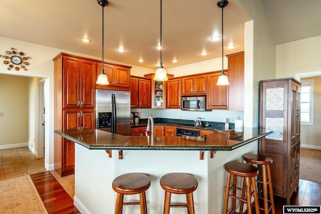 kitchen with a peninsula, a sink, hanging light fixtures, appliances with stainless steel finishes, and brown cabinets