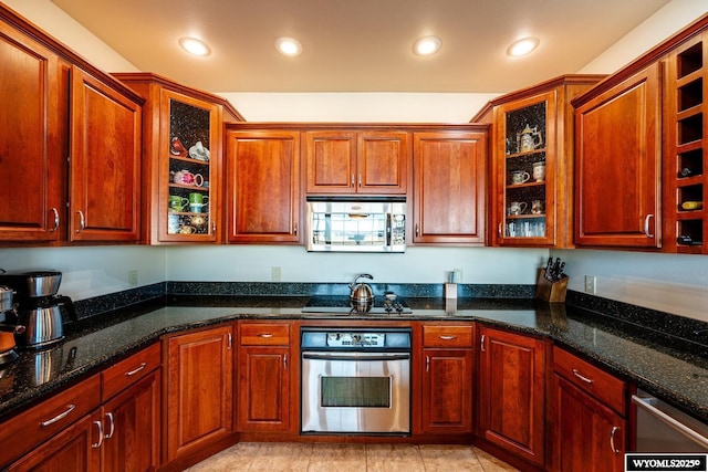 kitchen with light tile patterned floors, recessed lighting, stainless steel appliances, dark stone counters, and glass insert cabinets