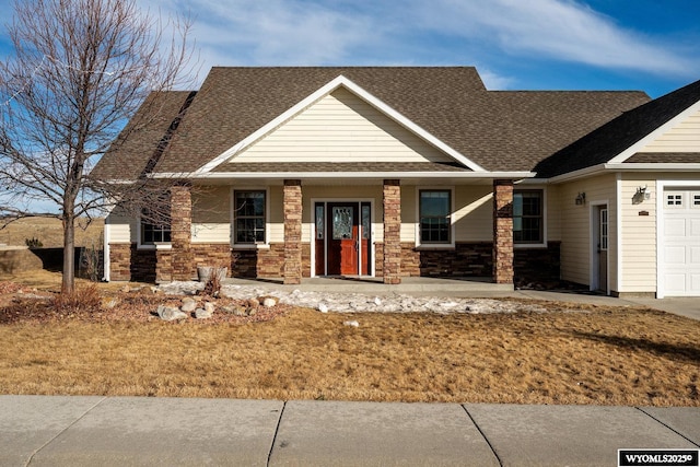 craftsman-style home with a shingled roof, covered porch, stone siding, and an attached garage