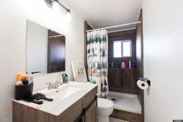 bathroom featuring toilet, curtained shower, a textured wall, and vanity