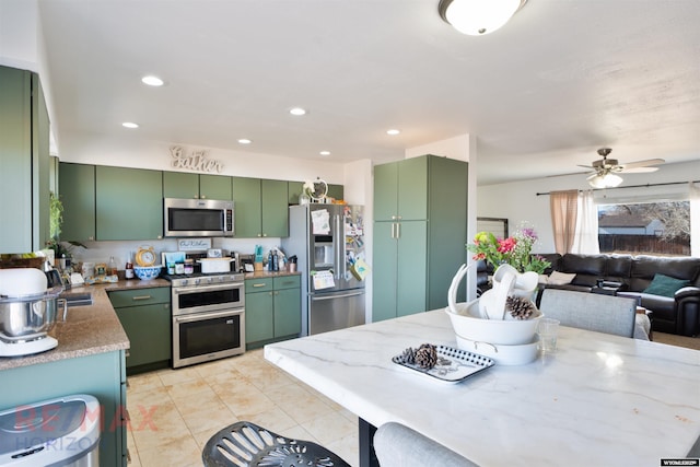 kitchen featuring stainless steel appliances, recessed lighting, green cabinets, open floor plan, and light stone countertops