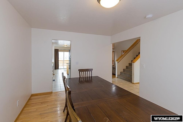 unfurnished dining area with light wood-style flooring, stairs, and baseboards