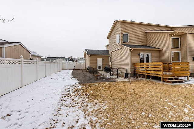 snow covered back of property with a patio, a fenced backyard, a wooden deck, and central air condition unit