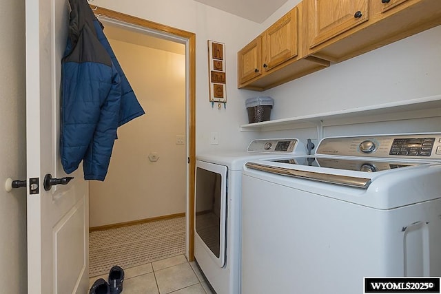 laundry area featuring light tile patterned floors, separate washer and dryer, cabinet space, and baseboards