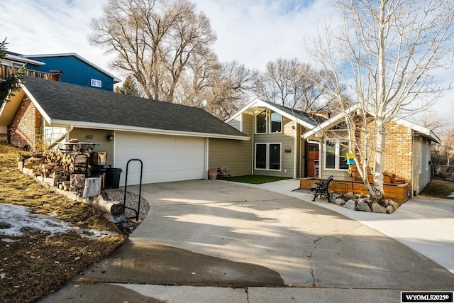 view of front of house featuring driveway, an attached garage, and a shingled roof