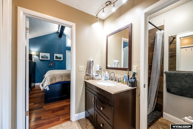 ensuite bathroom featuring a textured ceiling, ensuite bathroom, wood finished floors, vanity, and baseboards