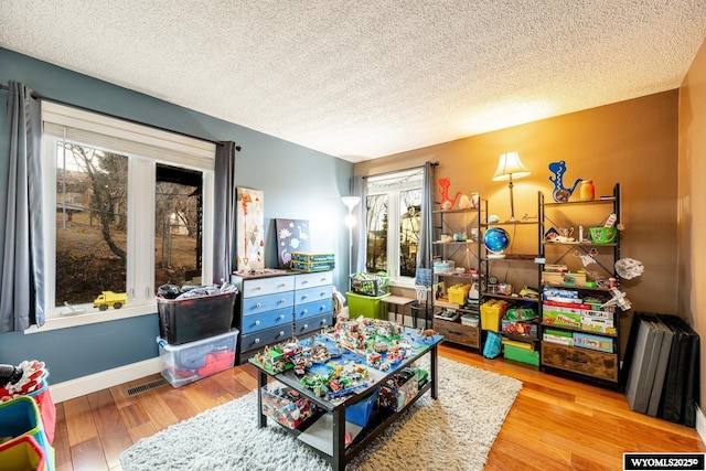 recreation room featuring visible vents, a textured ceiling, baseboards, and wood finished floors