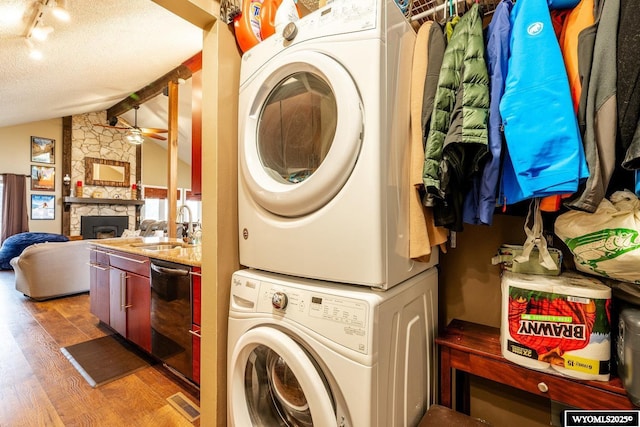 clothes washing area featuring light wood finished floors, laundry area, stacked washer / dryer, a fireplace, and a sink