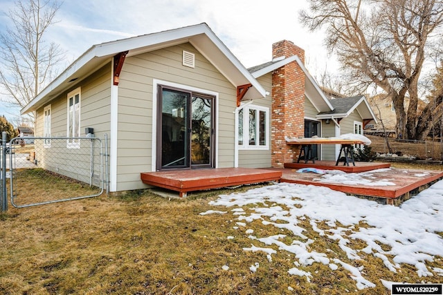 snow covered back of property featuring a yard, a chimney, a gate, fence, and a deck