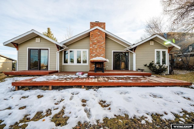 snow covered rear of property featuring french doors, a chimney, and a wooden deck