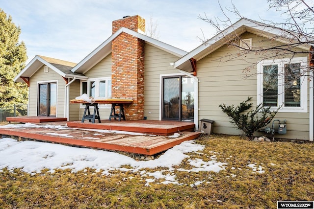 snow covered house featuring a deck and a chimney