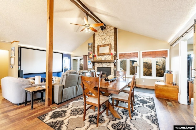 dining area with a textured ceiling, beamed ceiling, a fireplace, and wood finished floors