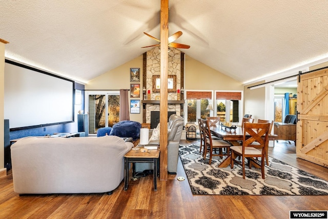 dining area with a textured ceiling, high vaulted ceiling, a barn door, a fireplace, and wood finished floors