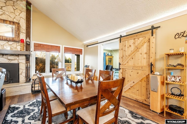 dining area featuring wood finished floors, a fireplace, a textured ceiling, and a barn door