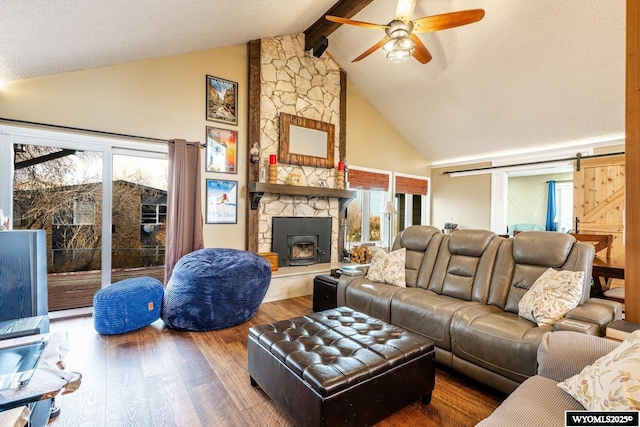 living area with a barn door, beamed ceiling, wood finished floors, and a healthy amount of sunlight