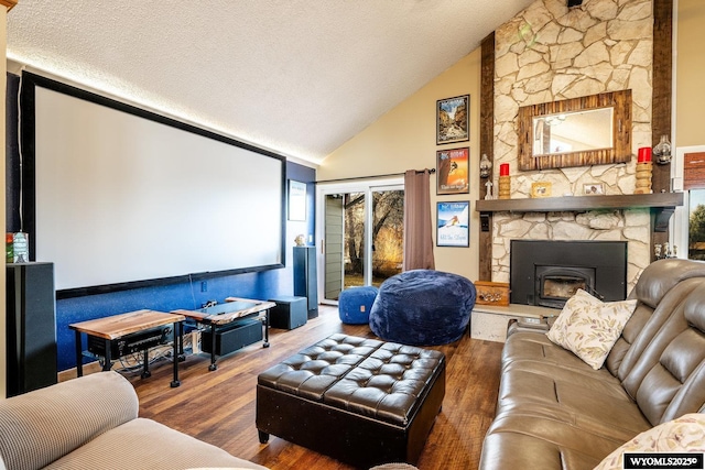 cinema with a textured ceiling, high vaulted ceiling, a stone fireplace, and wood finished floors