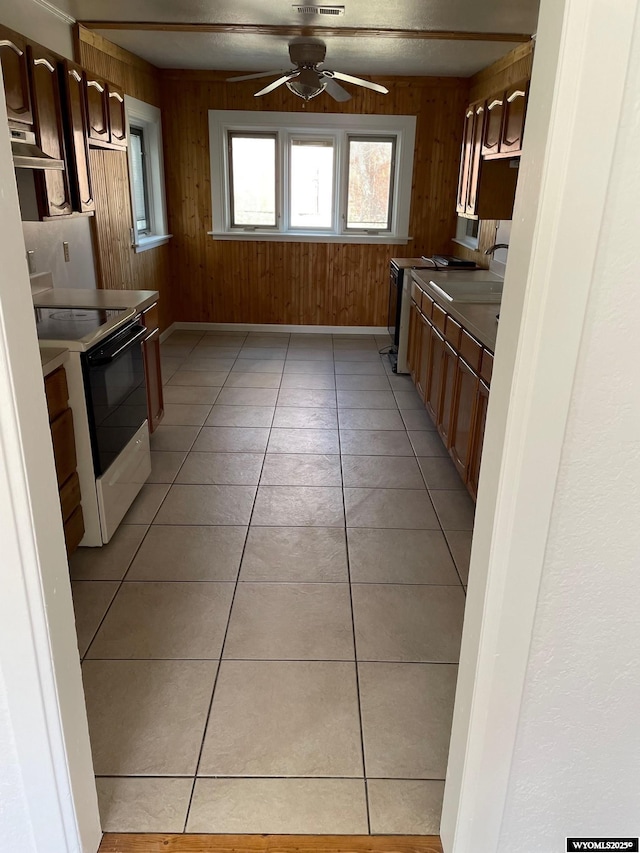 kitchen featuring light tile patterned floors, under cabinet range hood, wood walls, a ceiling fan, and electric range oven