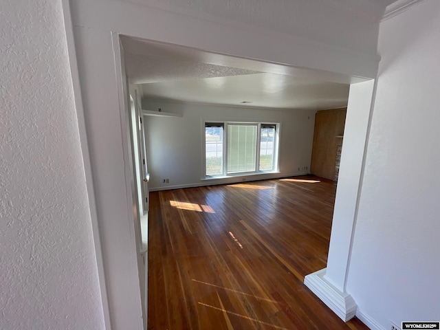 empty room featuring baseboards, dark wood-style flooring, and a textured wall