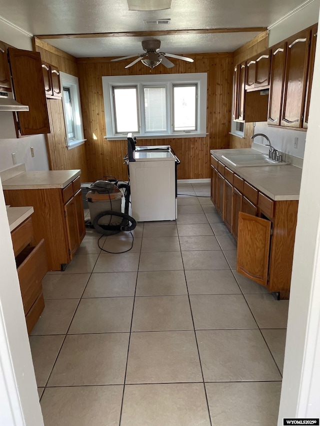 kitchen with a ceiling fan, light tile patterned flooring, a sink, wooden walls, and under cabinet range hood