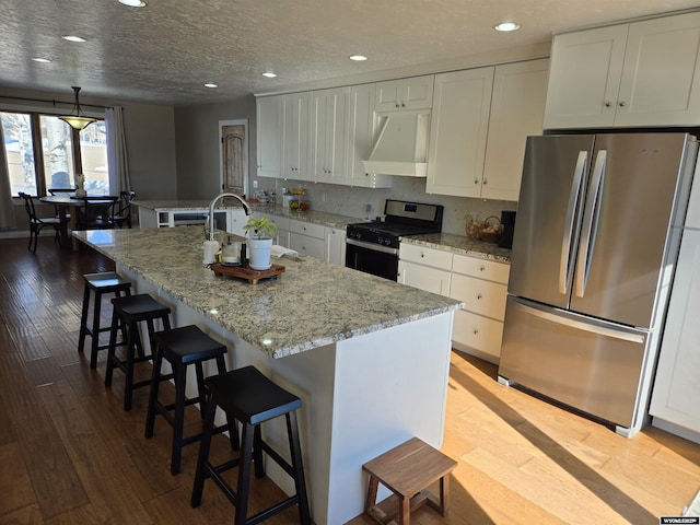 kitchen with range hood, stainless steel appliances, white cabinetry, a sink, and wood finished floors