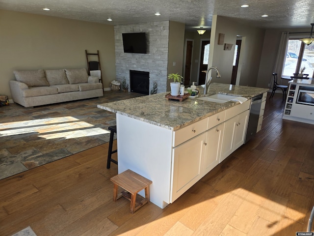 kitchen with white cabinets, dishwasher, dark wood-type flooring, a stone fireplace, and a sink