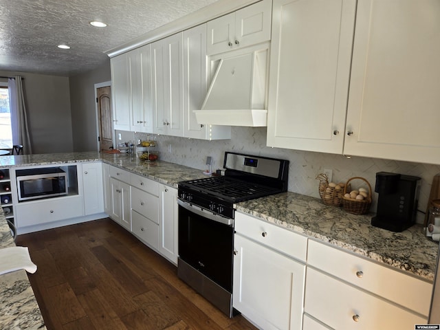 kitchen with dark wood-style flooring, appliances with stainless steel finishes, white cabinetry, a textured ceiling, and a peninsula