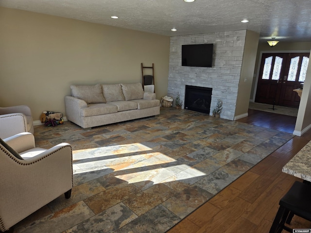 living area with a fireplace, baseboards, a textured ceiling, and wood finished floors