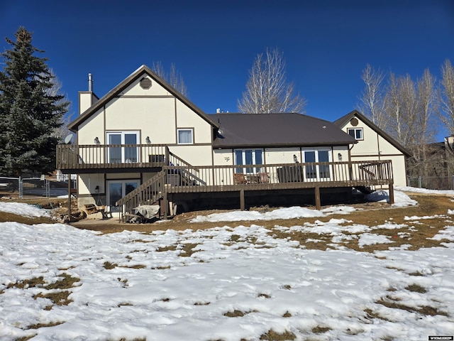 snow covered house with a chimney, fence, stairway, and a wooden deck