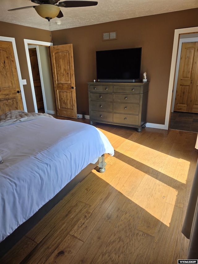 bedroom featuring a ceiling fan, a textured ceiling, baseboards, and wood finished floors