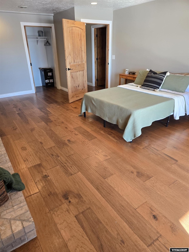 bedroom with a closet, baseboards, a textured ceiling, and hardwood / wood-style floors