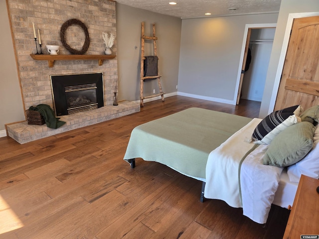 bedroom featuring a fireplace, a textured ceiling, baseboards, and wood finished floors