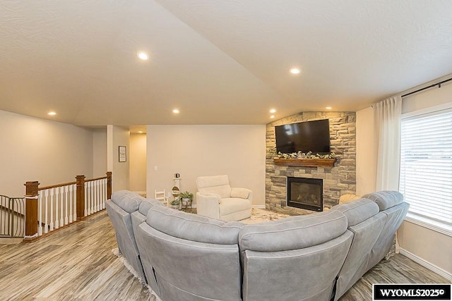 living area featuring lofted ceiling, a stone fireplace, light wood-style flooring, recessed lighting, and baseboards